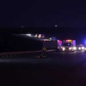 Scene of a car crash on a highway at nighttime surrounded by emergency responders.